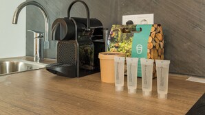 Keittiöalue, jossa on kahvinkeitin, puinen säiliö ja kolme The Spa Collection -sarjan tuotetta sisältävää pakkausta puisen työtason päällä.
