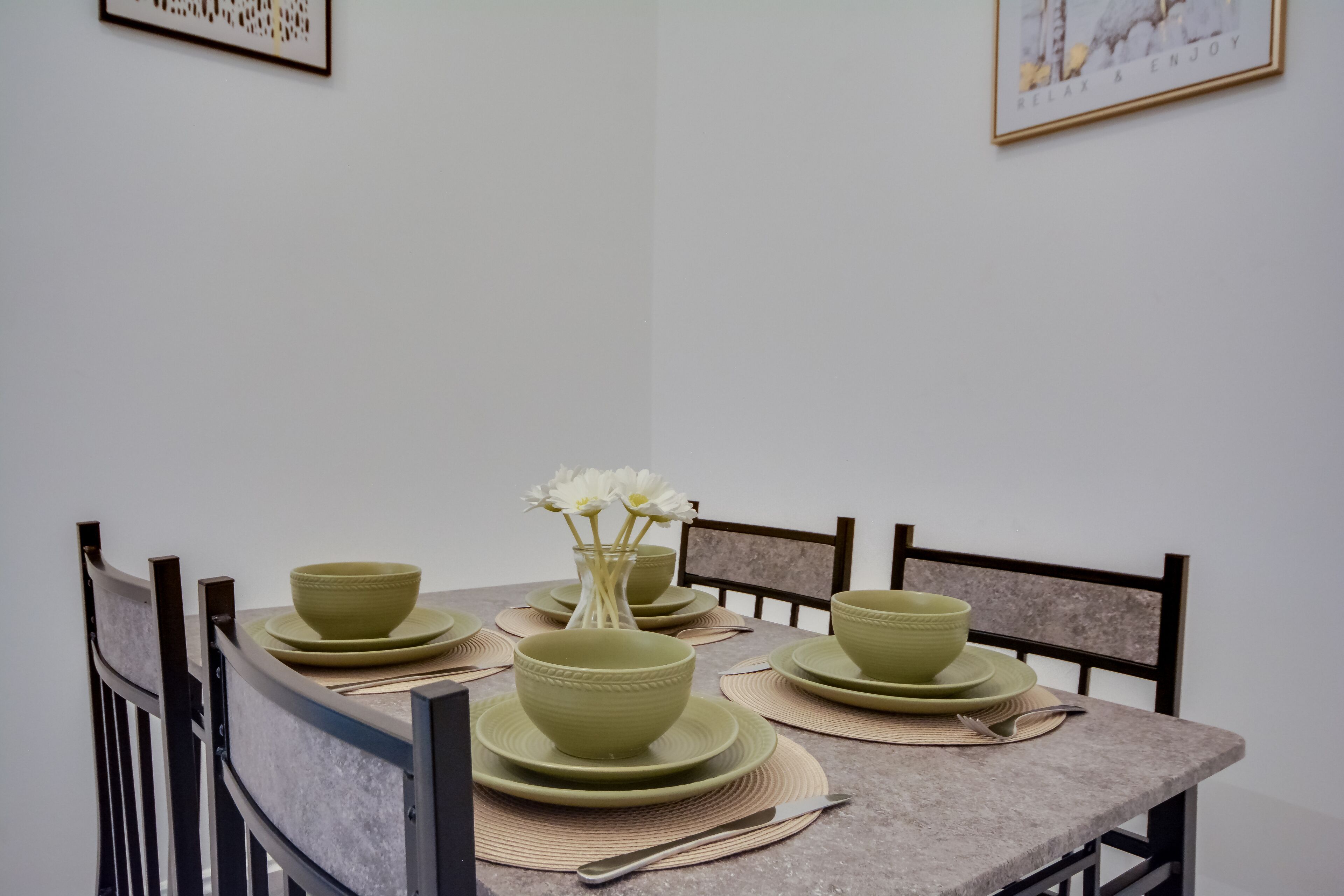 Ein Esstisch, gedeckt mit grünen Schüsseln und Tellern, eine Vase mit weißen Blumen und ein gerahmtes Bild an der Wand.