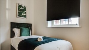 Un lit bien fait, avec une tête de lit sombre, un oreiller blanc et un plaid vert.