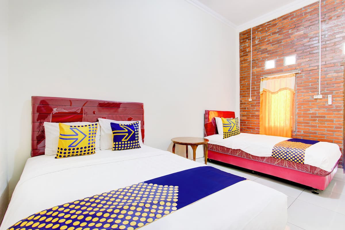 A hotel room with a red headboard, two beds with patterned bedding, a small round table, and a brick wall with a window.