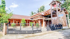 Un bâtiment en briques de deux étages, avec un toit recouvert de tuiles rouges, une entrée fermée par un portail et une enseigne indiquant « SHINTA ».