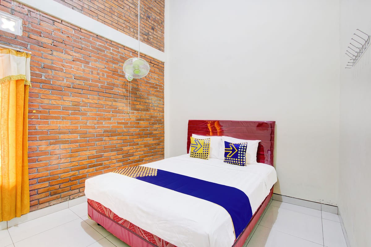 A hotel room with a brick wall, a bed with a red headboard, and a white ceiling fan.