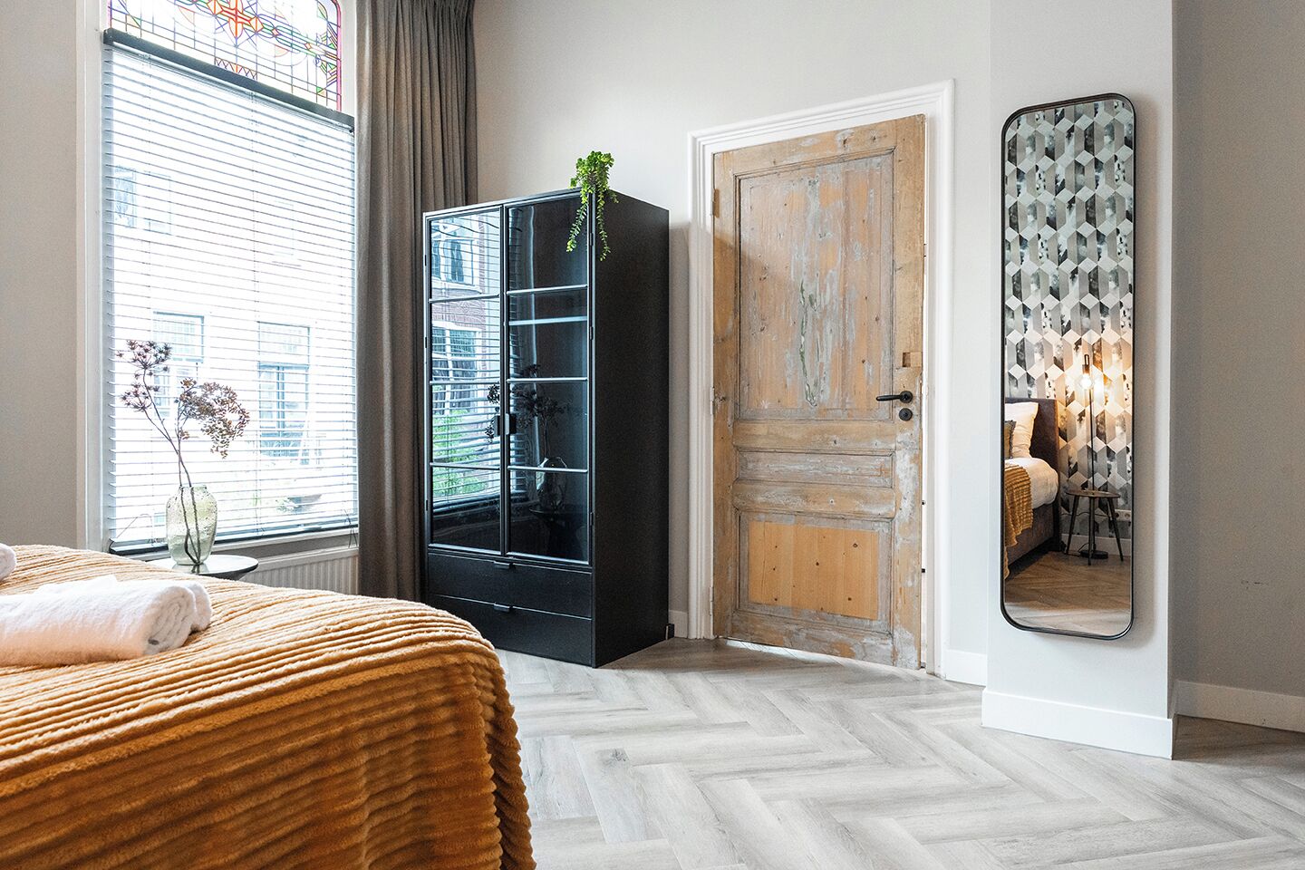 A bedroom with a bed, a wardrobe, a door, and a mirror.