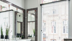 A modern bathroom with a large mirror, white cabinetry, and a view of buildings through a window with blinds. - Cozy 35m² apartment with bath, fast WiFi, and charming herringbone floors. Perfect for a relaxing stay or business trip in the heart of Tilburg. (Tilburg)