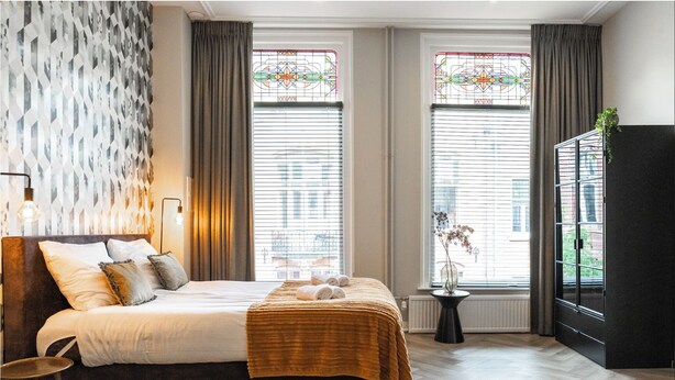 A hotel room with a bed, a small table, a potted plant, and a cabinet. - Cozy 35m² apartment with bath, fast WiFi, and charming herringbone floors. Perfect for a relaxing stay or business trip in the heart of Tilburg. (Tilburg)