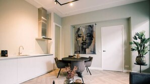 Een moderne keuken met witte kasten, een eethoek met een ronde tafel en stoelen, en een groot abstract schilderij aan de muur.