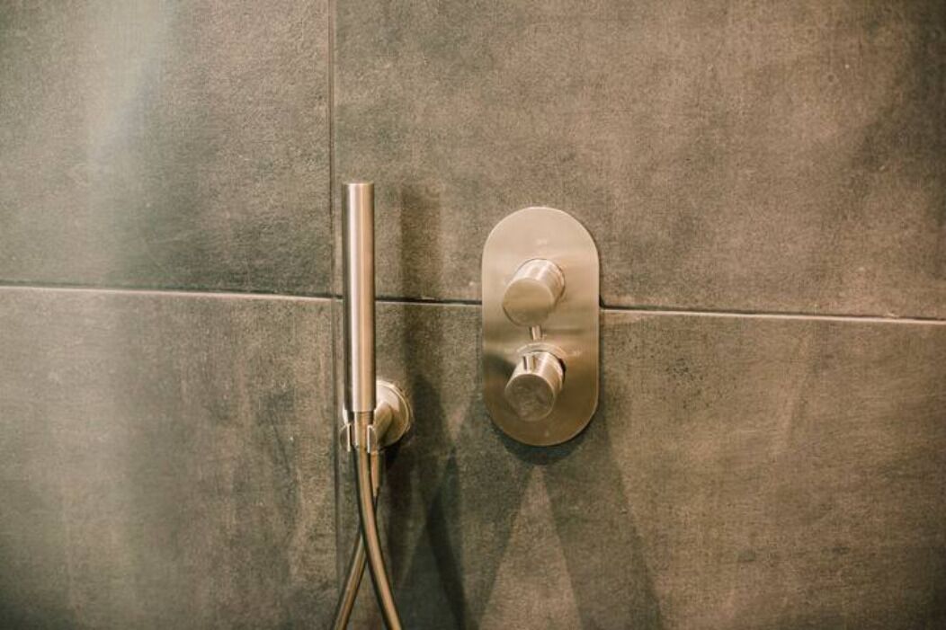 Een douchepaneel met een handdouche en een bedieningsknop aan de muur.