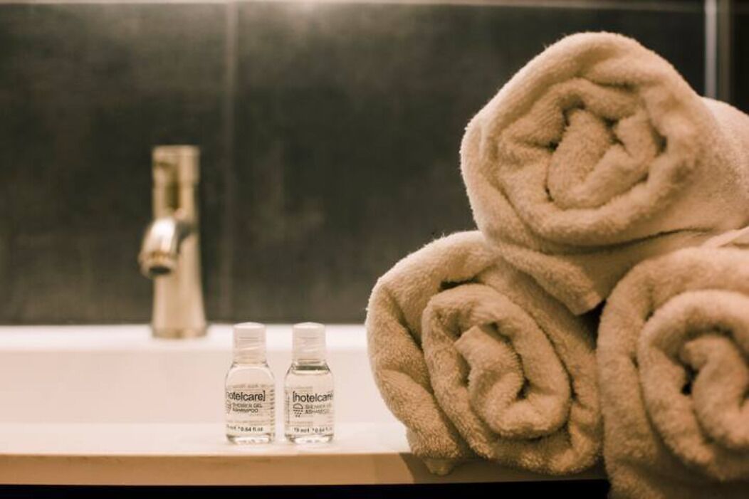 A bathroom with a sink, two bottles of hotel care products, and rolled towels.
