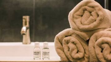 A bathroom with a sink, two bottles of hotel care products, and rolled towels.