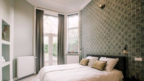 Een slaapkamer met een groot bed, een radiator, een raam met gordijnen en een wand met een patroon.
