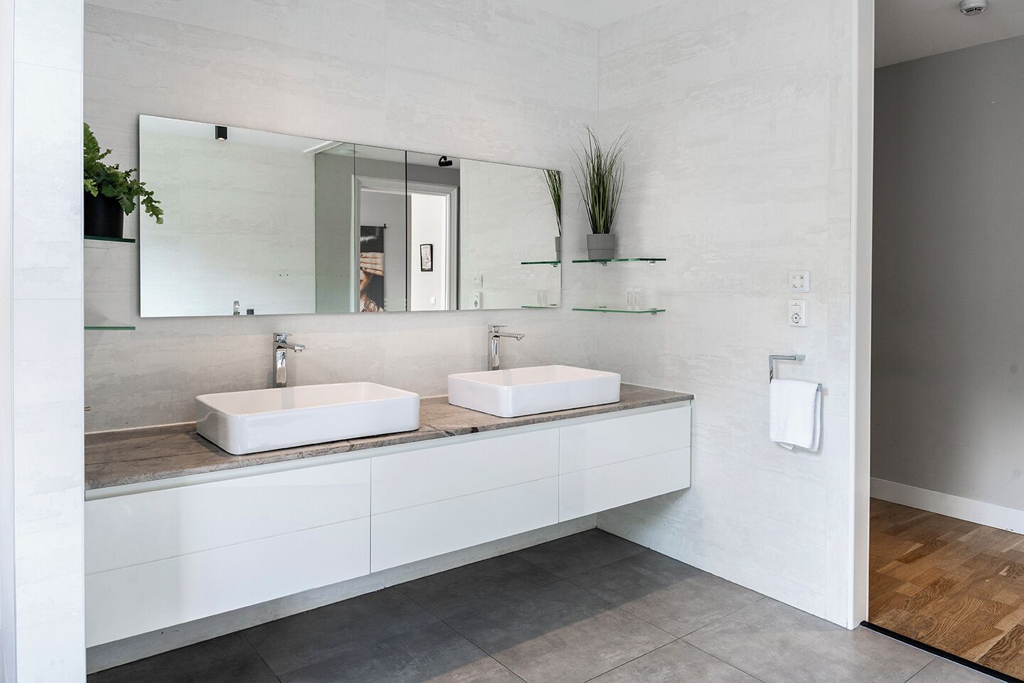 Een moderne badkamer met twee witte wasbakken, een grote spiegel en een plantje op een plank.