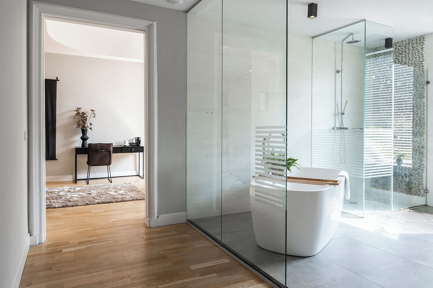 Un baño moderno con cabina de ducha de vidrio, bañera blanca y suelo de madera.