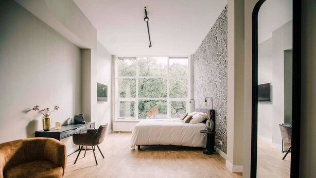 A modern bedroom with a large window, a bed, a desk, and a chair. - First-floor suite, 35m2, ensuite bathroom with bath and rain shower. (Tilburg)