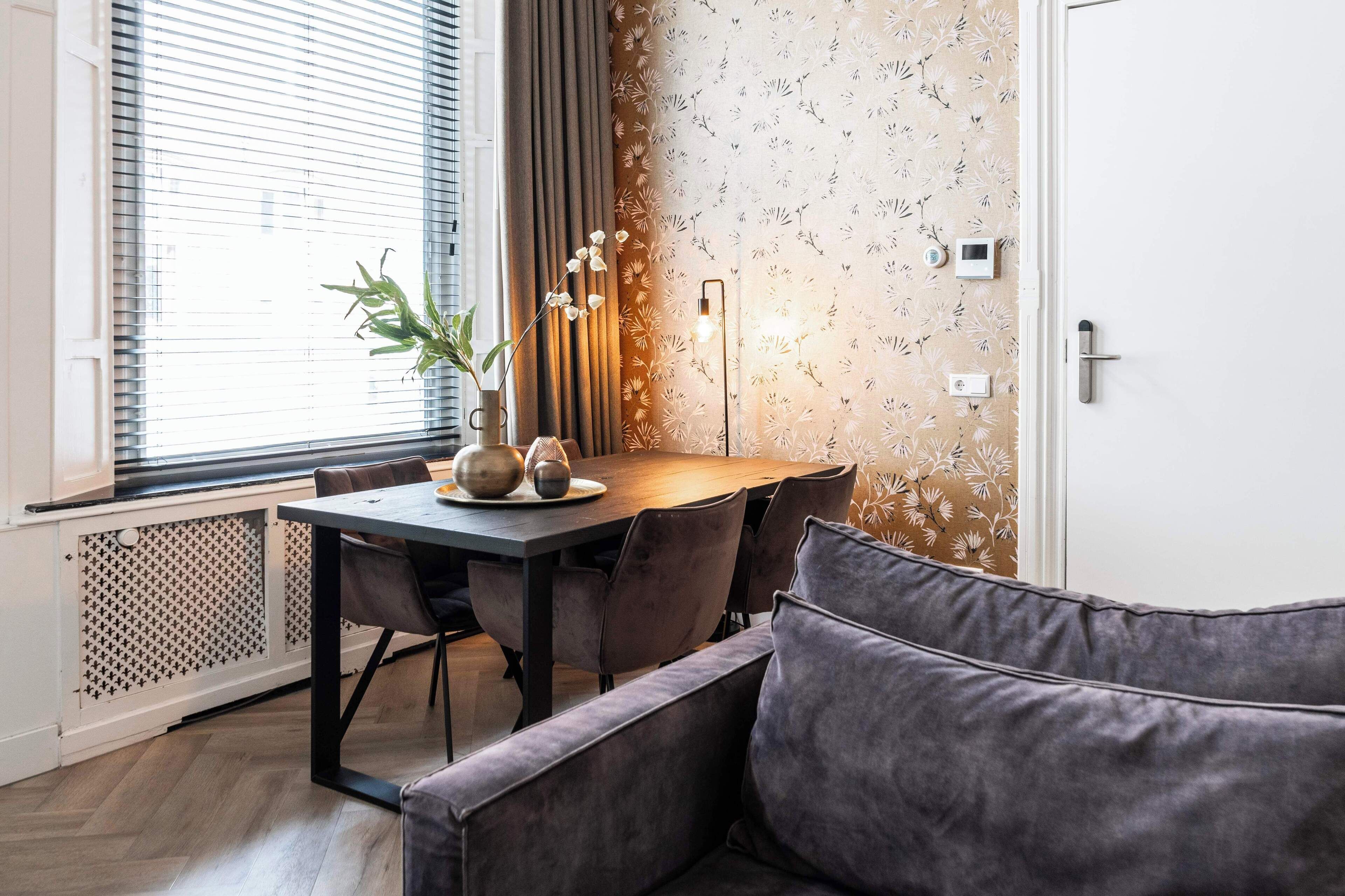 Een moderne eethoek met een houten tafel, grijze bekleden stoelen en een grijze bank.