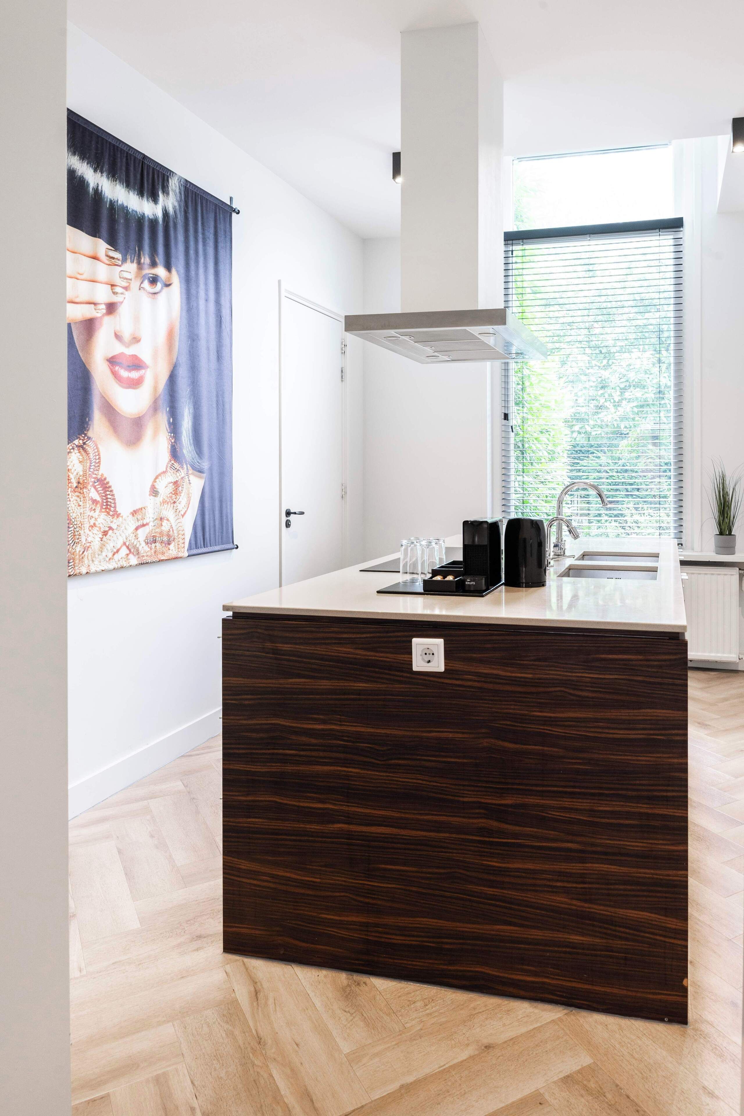 A modern kitchen with a wooden island, a coffee maker, and a window with blinds.