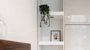 Una estantería blanca con una planta, un cuadro enmarco, platos apilados y un cuenco de madera.