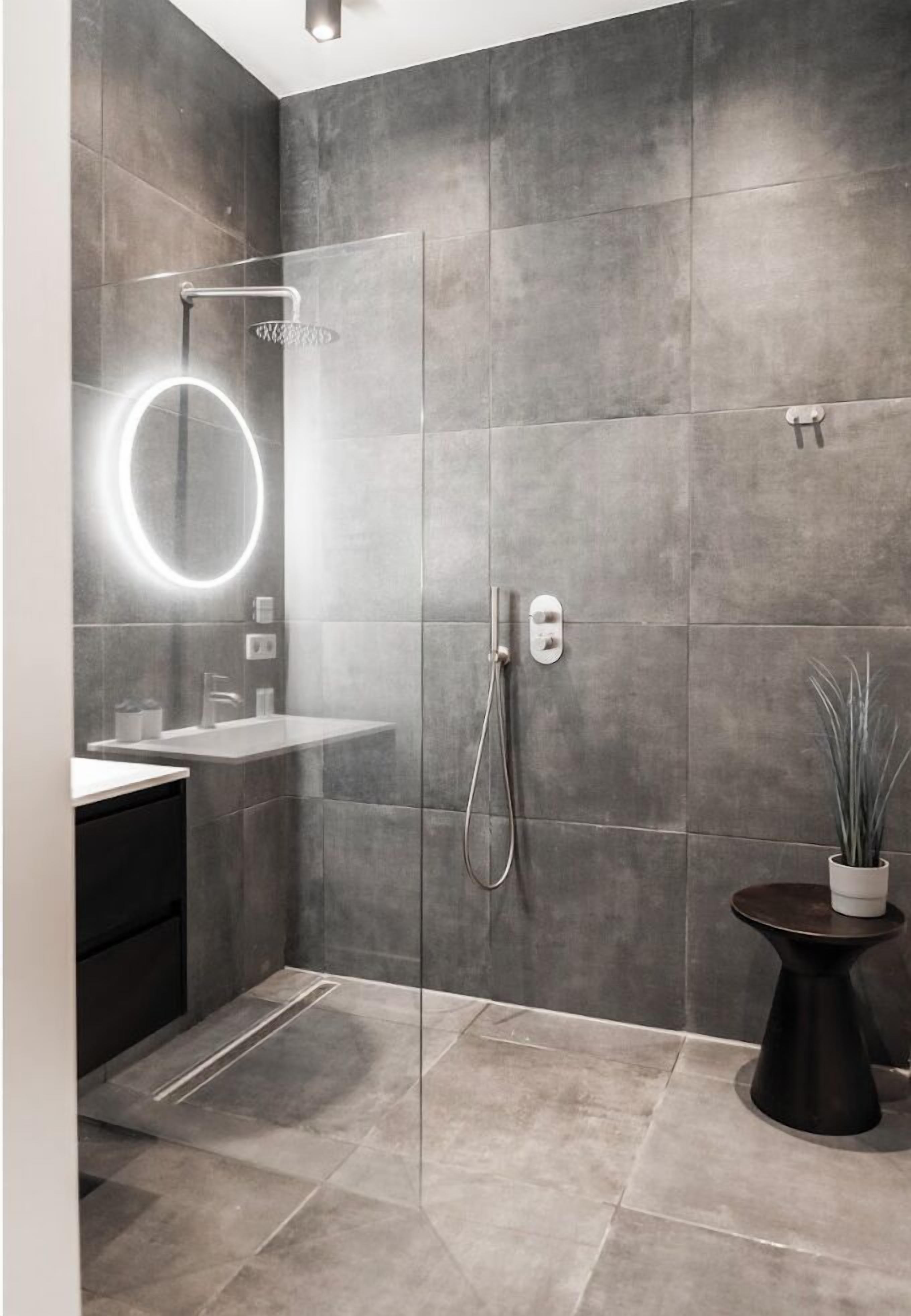 Een moderne badkamer met een douchecabine van glas, een ronde spiegel en een kleine pot met een plantje.