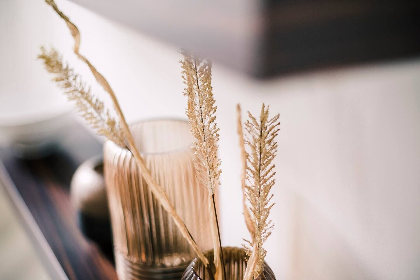 A clear view of a vase with dried grass stems, placed on a surface with a blurred background.