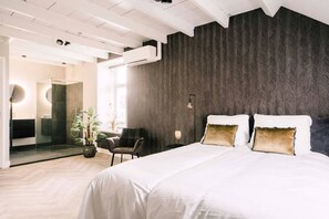 A modern bedroom with a large bed, a chair, a potted plant, and a bathroom visible through a glass door. - Experience comfort and convenience at Bed en Koffie, located in the heart of Tilburg Centrum. Perfect for business travelers or couples looking to Efteling overnachten or appartement huren Tilburg. (Tilburg)