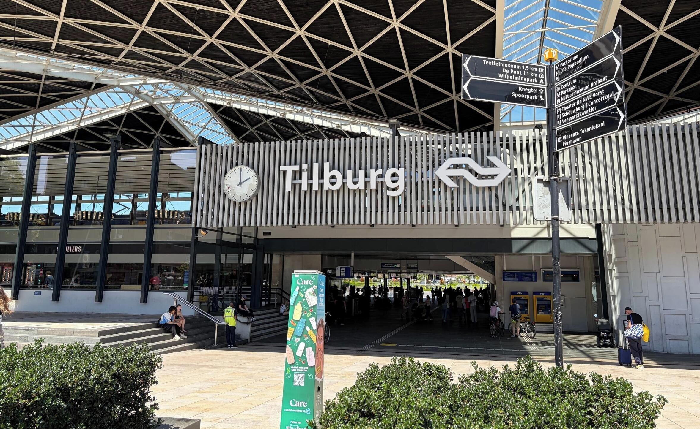 A modern building with a prominent clock and directional signs, indicating a public transportation hub.