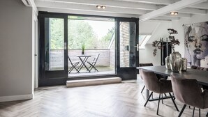 A modern dining area with a large table and chairs, a view of the outdoors through a sliding glass door, and a contemporary art piece on the wall.