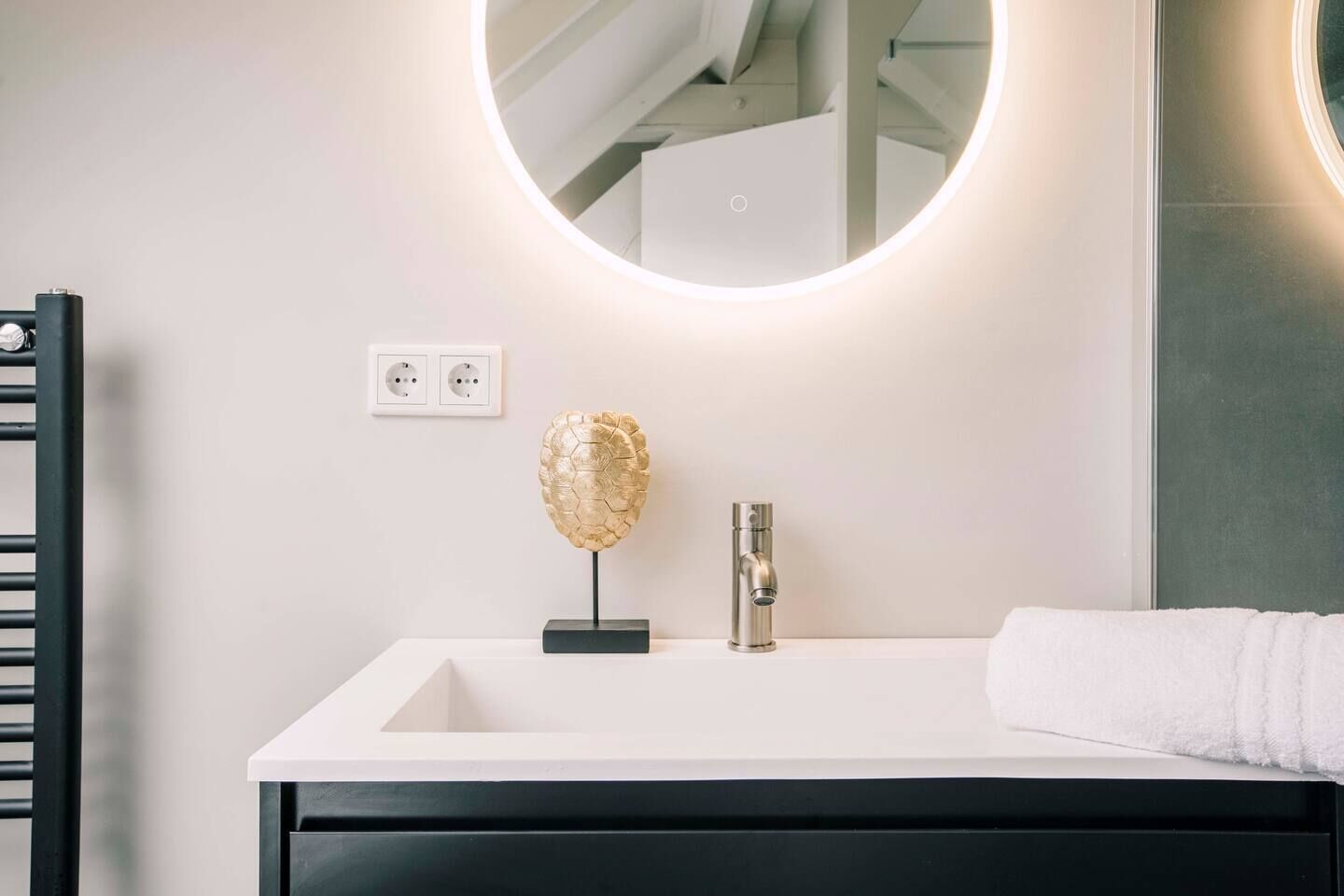 Een moderne badkamer met een wit badkamermeubel, een gouden decoratie en een ronde spiegel met ingebouwde verlichting.