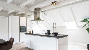 A modern kitchen with white cabinetry, a central island, a stainless steel range hood, and a skylight.