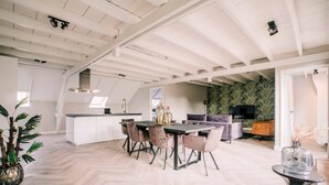 A spacious loft with a high ceiling, a dining area with a herringbone floor, and a cozy seating area with a television.
