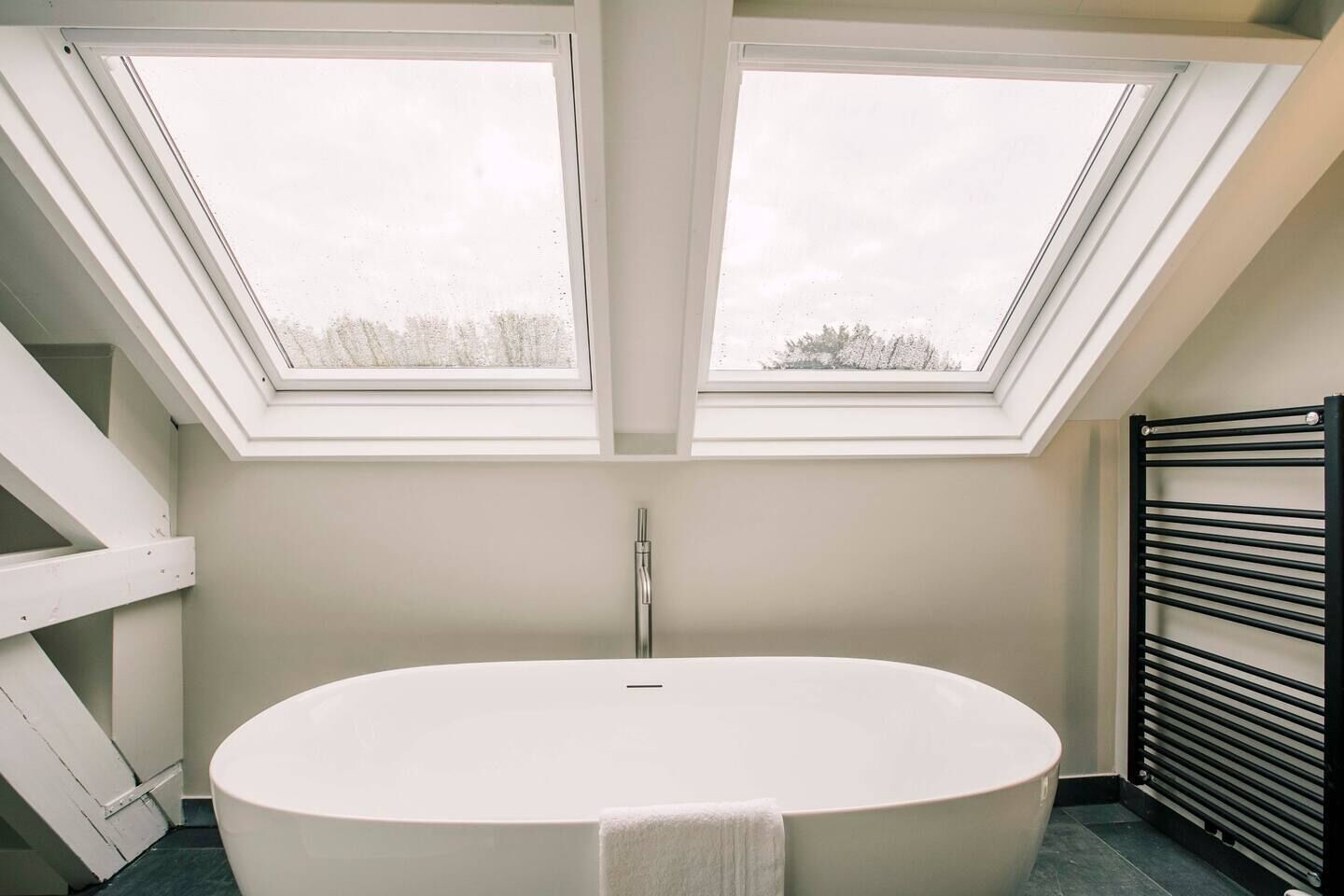 A modern bathroom with a freestanding bathtub, skylights, and a radiator.