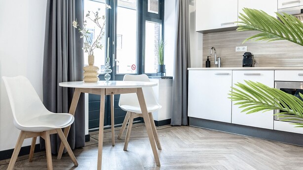 Una cocina moderna con armarios blancos, una mesa redonda de madera y dos sillas blancas.