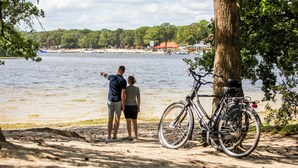 Una pareja está de pie junto a un lago, con una bicicleta estacionada cerca.