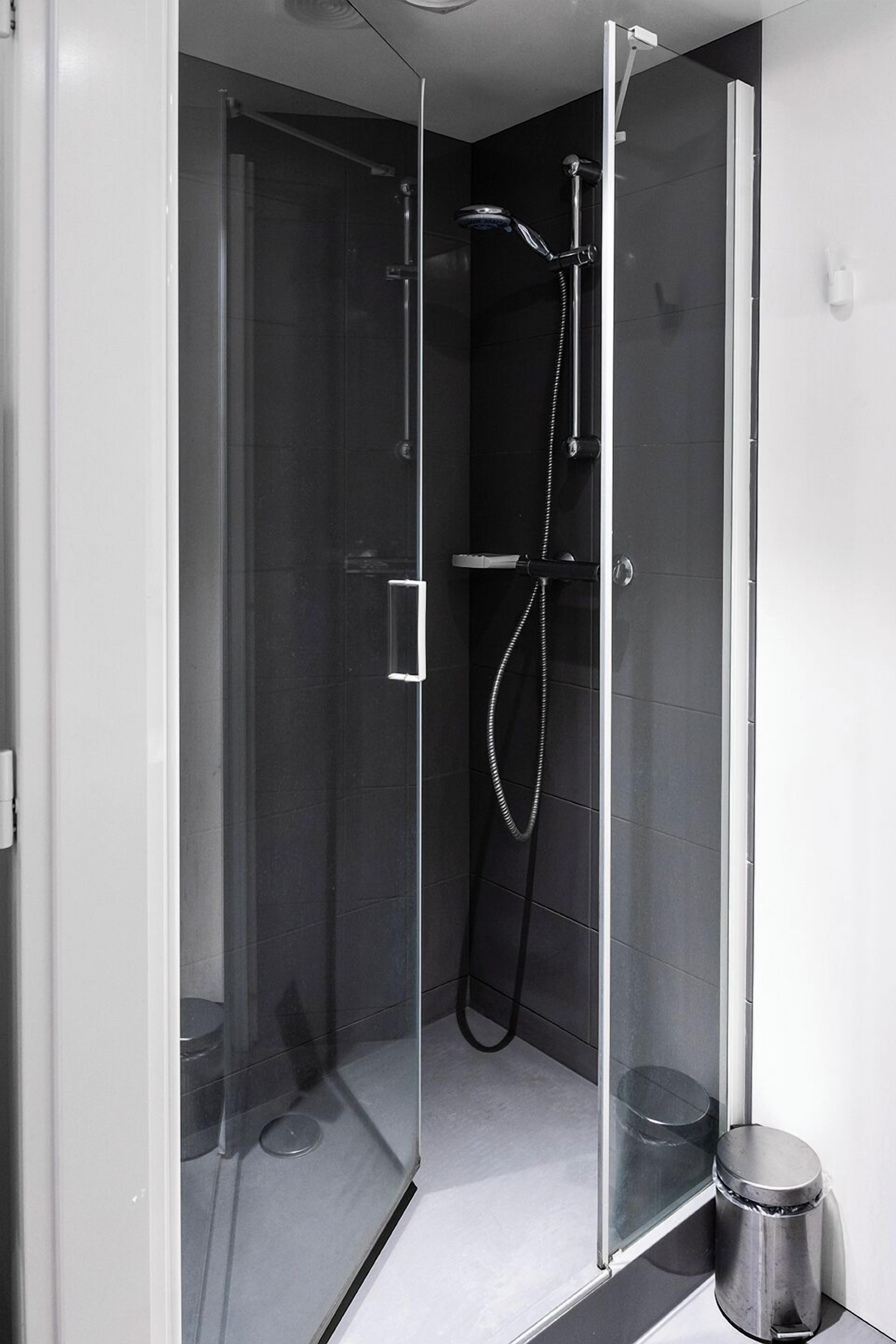 A modern shower enclosure with a glass door, a handheld showerhead, and a wall-mounted faucet.