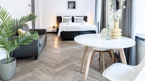 Una habitación de hotel moderna con cama, sofá, mesa de comedor y una planta en maceta.