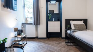 Un dormitorio moderno con cama, mesita de noche y un pequeño escritorio con lámpara.