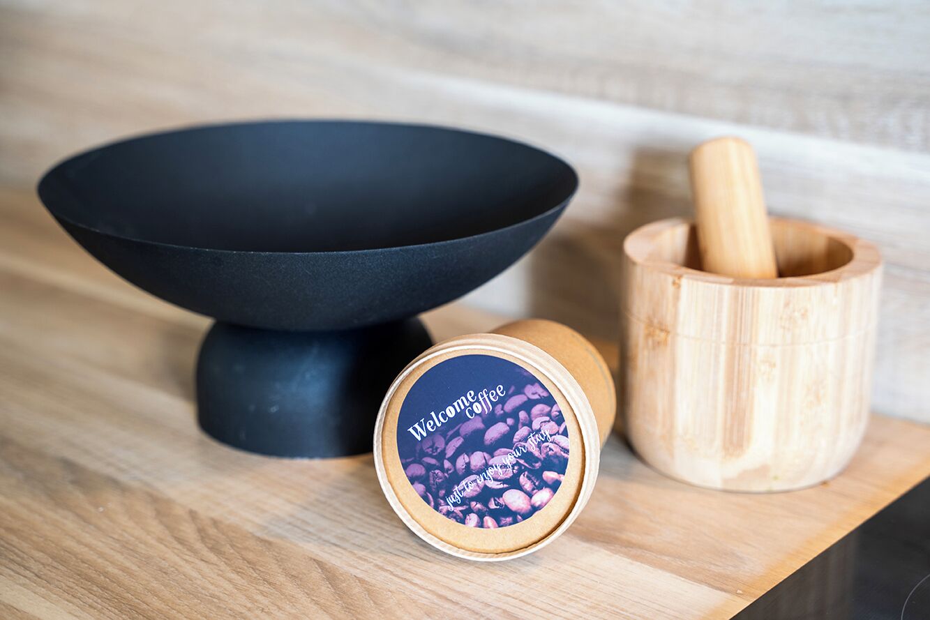 A kitchen counter with a black bowl, a wooden mortar and pestle, and a tin of coffee beans.