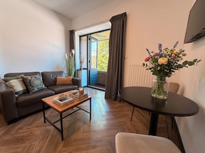 A living room with a sofa, coffee table, and a dining table with a vase of flowers.