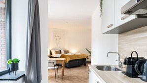 A modern kitchen with a sink, stove, and black coffee maker. A bed with a yellow blanket is visible in the background. - Modern space studio apartments near Hotel Central, ideal for lovers of refinement. (Tilburg)