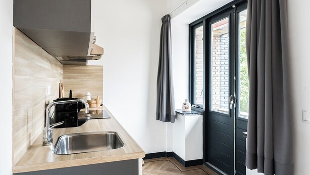 A compact kitchen with a sink, a stove, and a window with curtains. - Modern space studio apartments near Hotel Central, ideal for lovers of refinement. (Tilburg)