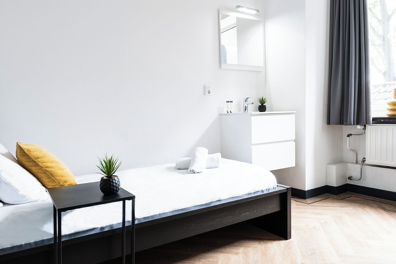 A modern bedroom with a bed, bedside table, and a small potted plant.