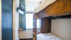 Habitación con literas, cabecero de madera, una ventana pequeña con cortinas y una puerta con pomo.