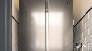 Un refrigerador Samsung de acero inoxidable con una garantía de 10 años, ubicado en una cocina con paredes de ladrillo blanco y pisos de mármol negro.