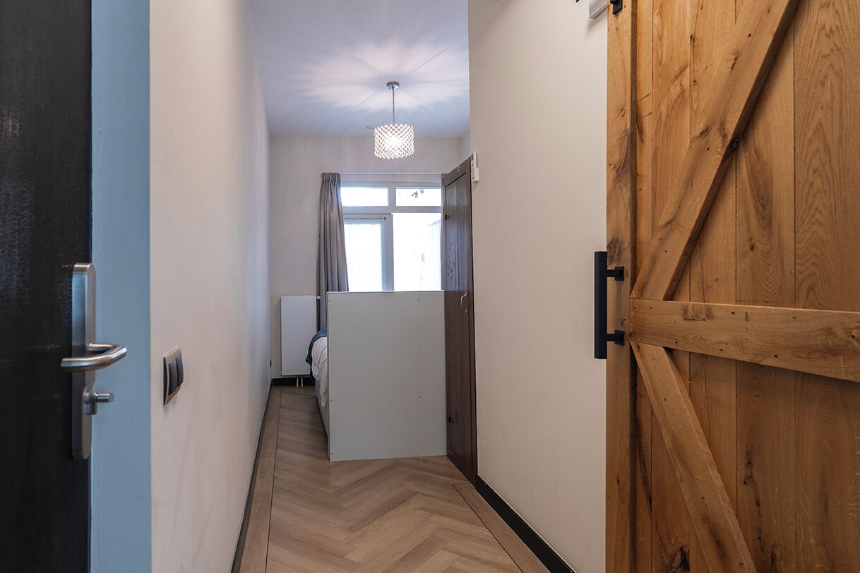 Un couloir avec une porte en bois, un mur blanc et une fenêtre avec des rideaux.