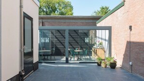 A modern outdoor patio with a glass door leading to a seating area with tables and chairs.