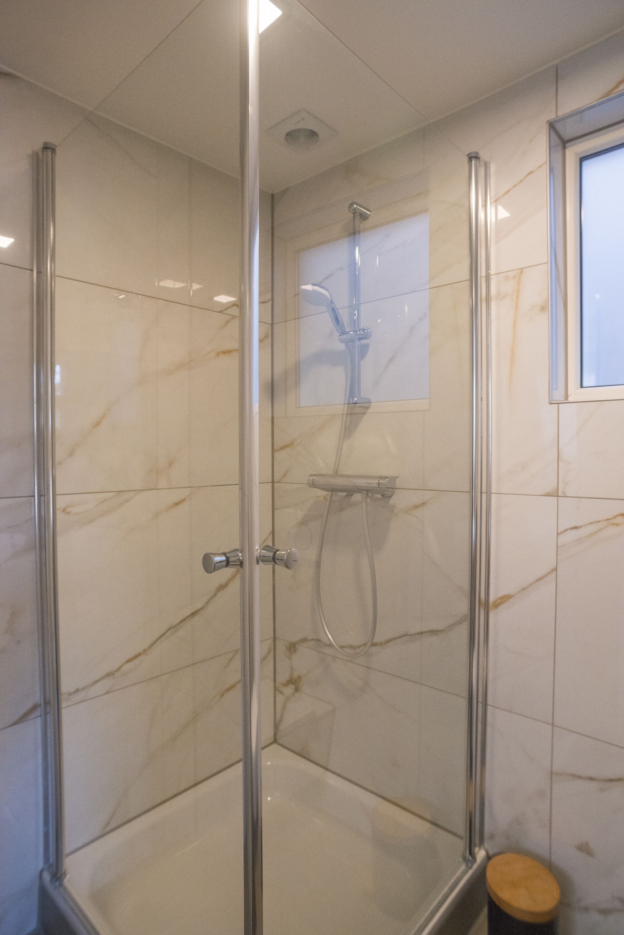 A glass-enclosed shower with a handheld showerhead and a wall-mounted faucet.