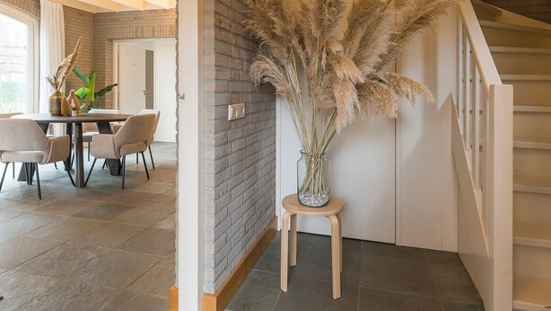 A spacious room with a dining area, a staircase, and a decorative vase with pampas grass. - Spacious countryside stay near Boxtel with lake views, free parking and fast Wi-Fi. Quiet, comfortable and perfect for a relaxing getaway. (Boxtel)