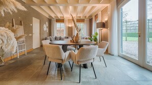A spacious dining area with a round table surrounded by chairs, a brick wall, and large windows offering a view of the outdoors. - Spacious countryside stay near Boxtel with lake views, free parking and fast Wi-Fi. Quiet, comfortable and perfect for a relaxing getaway. (Boxtel)