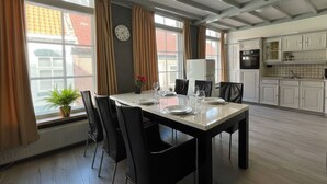 Un coin repas avec une table dressée pour quatre personnes, entourée de chaises, dans une cuisine moderne aux armoires blanches et où une horloge est visible au mur.