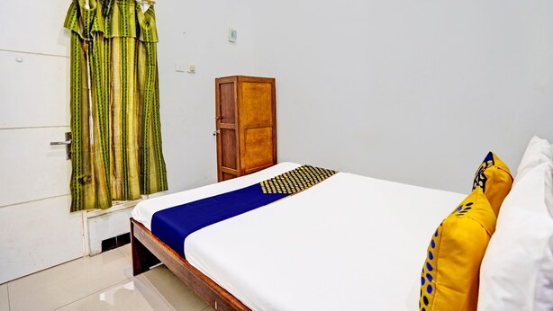 A bedroom with a bed, a wooden wardrobe, and green curtains. - Capital O 93854 Apartemen Sayana By Sentra Jaya (Tarumajaya)