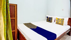 A single bed with a blue and white bedspread, two pillows with yellow and blue patterns, and a wooden wardrobe. - Capital O 93854 Apartemen Sayana By Sentra Jaya (Tarumajaya)