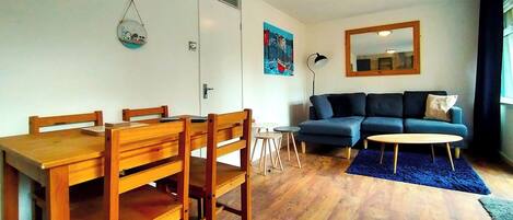 Sala de estar com mesa de jantar de madeira, sofá azul e mesa de centro redonda.